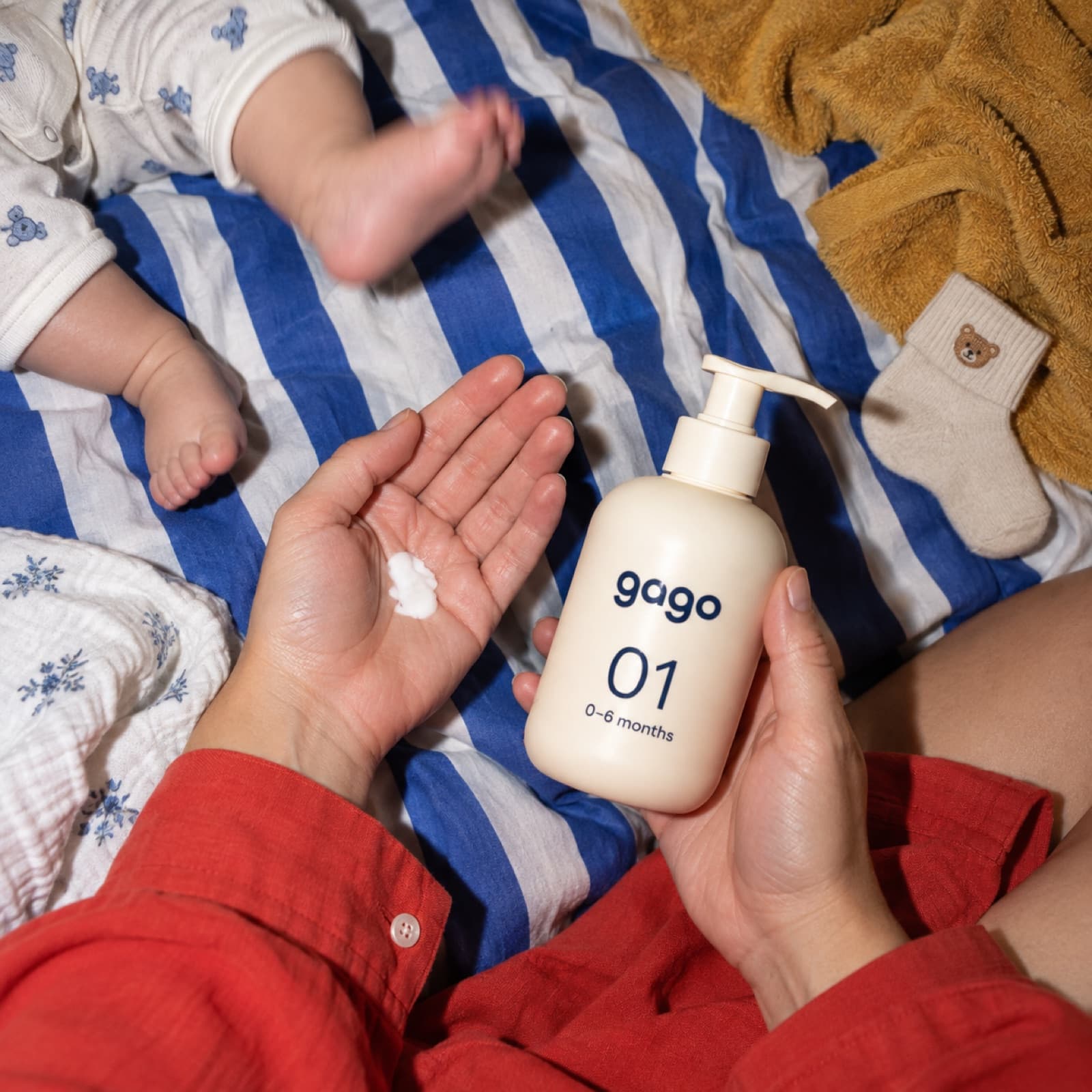 A parent holding the GaGo Stage 1 bottle beside a newborn on a striped blanket